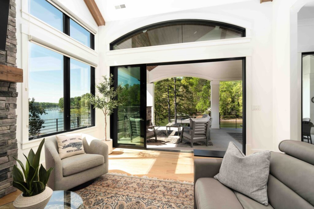 Views Of Lake And Forest Through Large Windows And Glass Sliders To Covered Porch